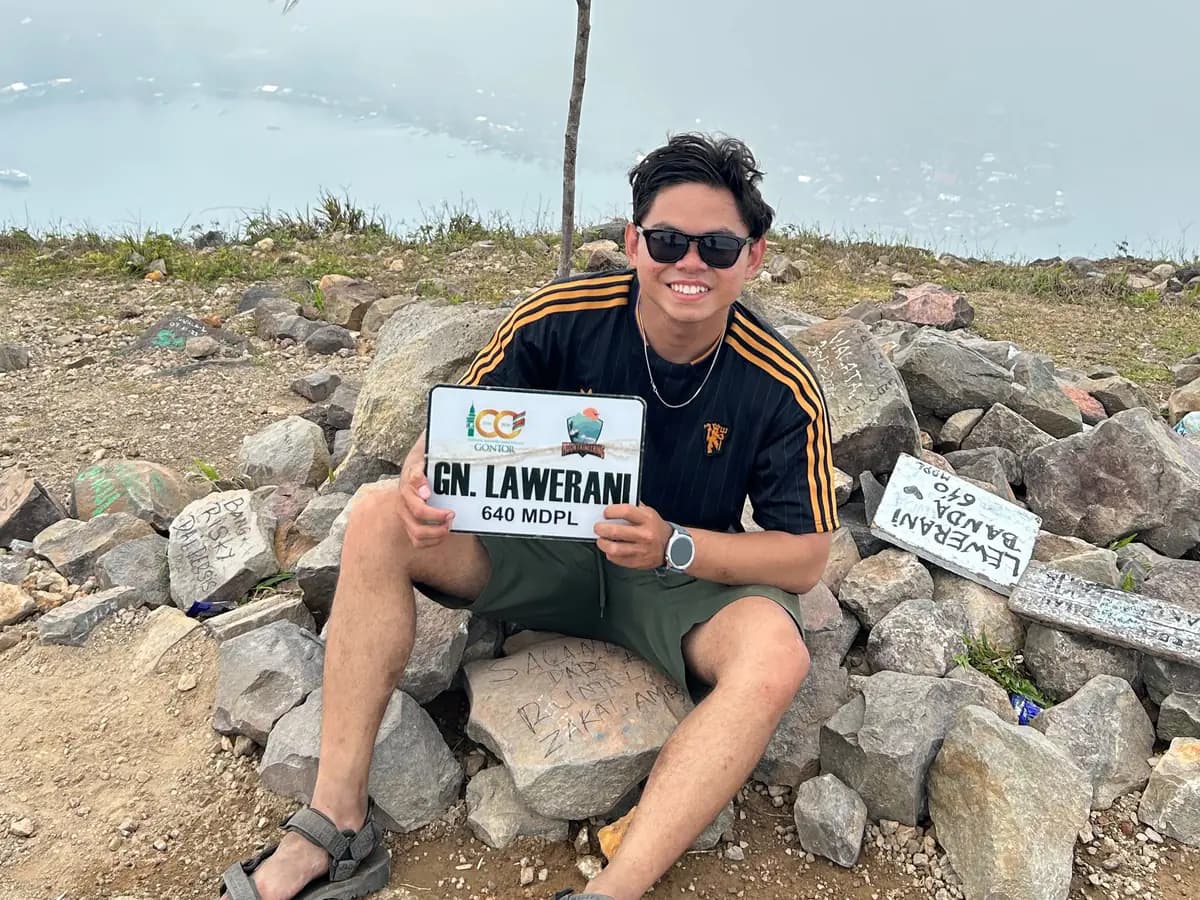Satriko on the summit cairn of Mount Api Banda, holding a summit sign